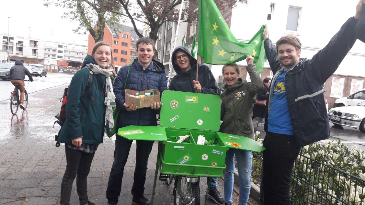 Fünf Menschen stehen um ein grünes Fahrrad mit Material für den Wahl·kampf