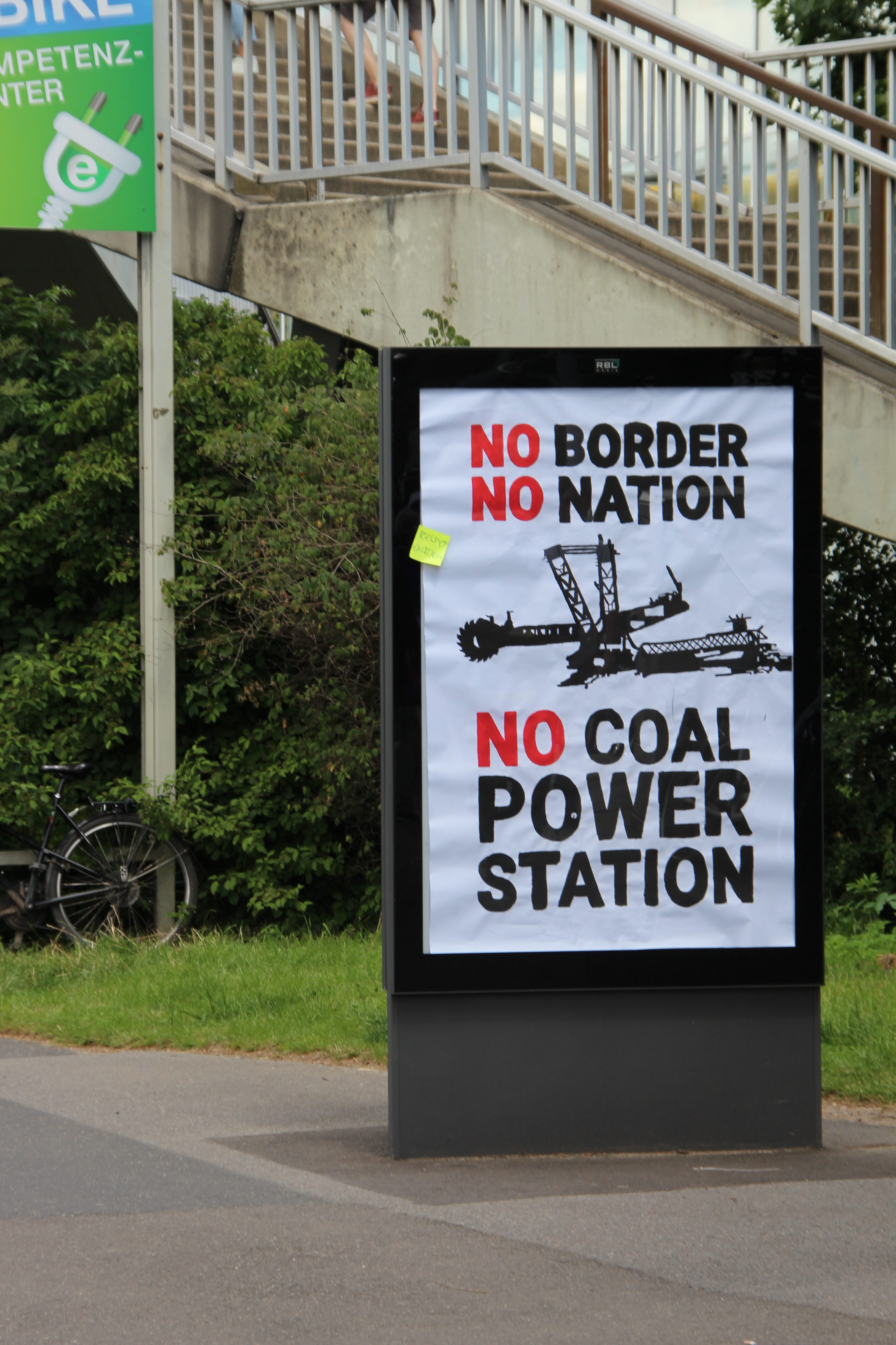In einem Plakat·ständer steht: "No Border, No Nation, No Coal Power Station:"