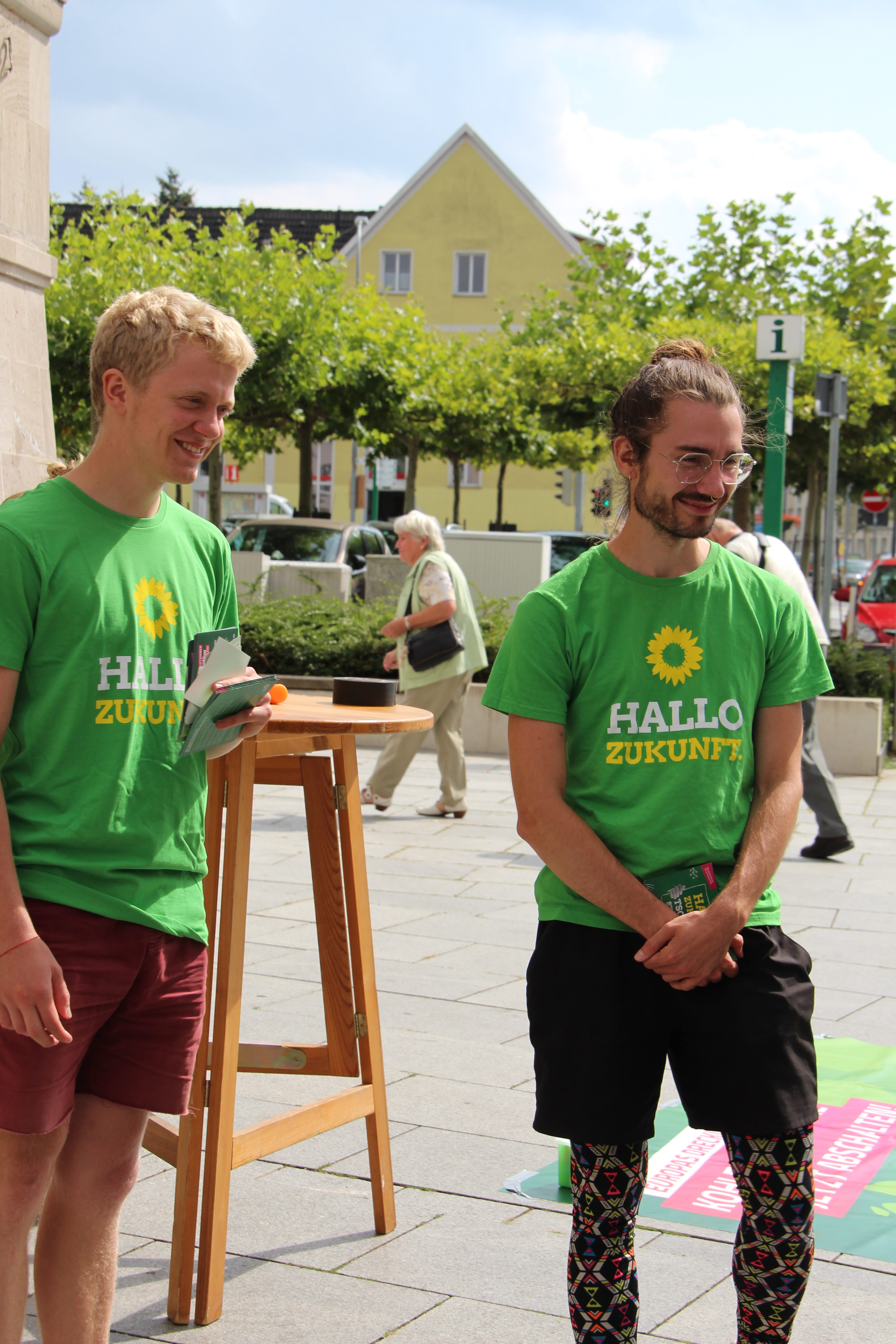 Zwei Menschen in Grünen T-Shirts stehen an einem Wahl·kampf·stand