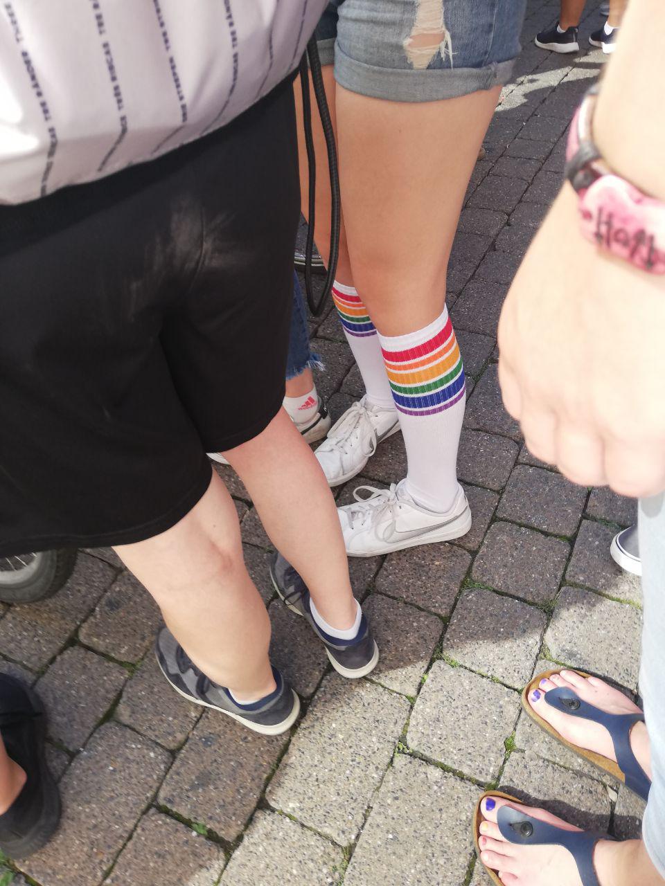 Ein Mensch trägt weiße Socken. Auf den Socken ist ein Regenbogen·muster.