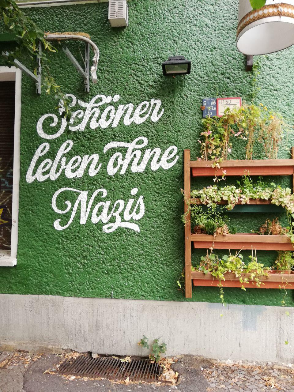 Auf dem Bild ist eine grüne Wand. Auf der Wand steht: "Schöner leben ohne Nazis."