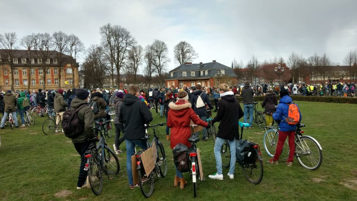 Viele Menschen stehen mit ihren Fahrrädern in einer Schlange. Sie unterhalten sich und warten