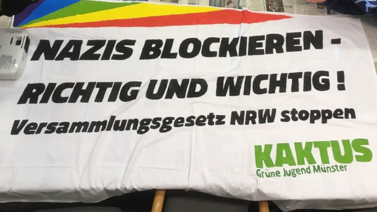 Ein Banner liegt auf einem Tisch. Auf dem Banner steht: Nazis blockieren - richtig und wichtig! Versammlungsgesetz NRW stoppen.
Unten in der Ecke ist das Logo der Grünen Jugend Münster